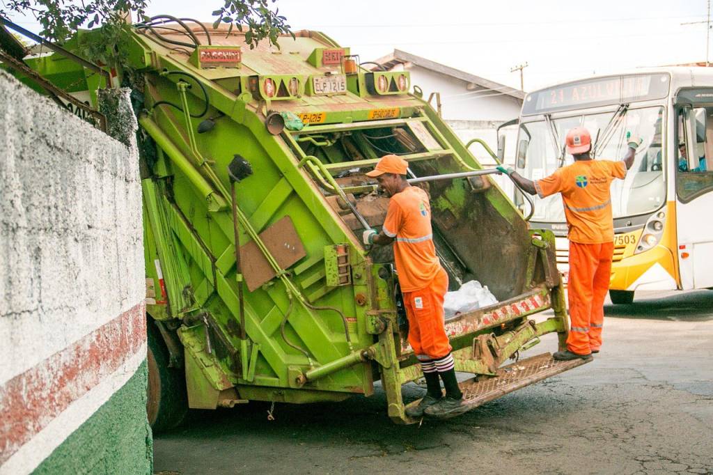 Sanitation workers providing garbage removal services Kent WA, loading waste into a green garbage truck on a city street.