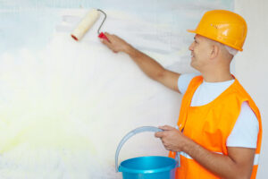 Professional painter in safety gear using paint roller on wall during home painting project