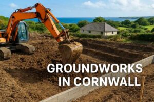 Excavator digging foundations on a construction site in Cornwall with sea and countryside views.